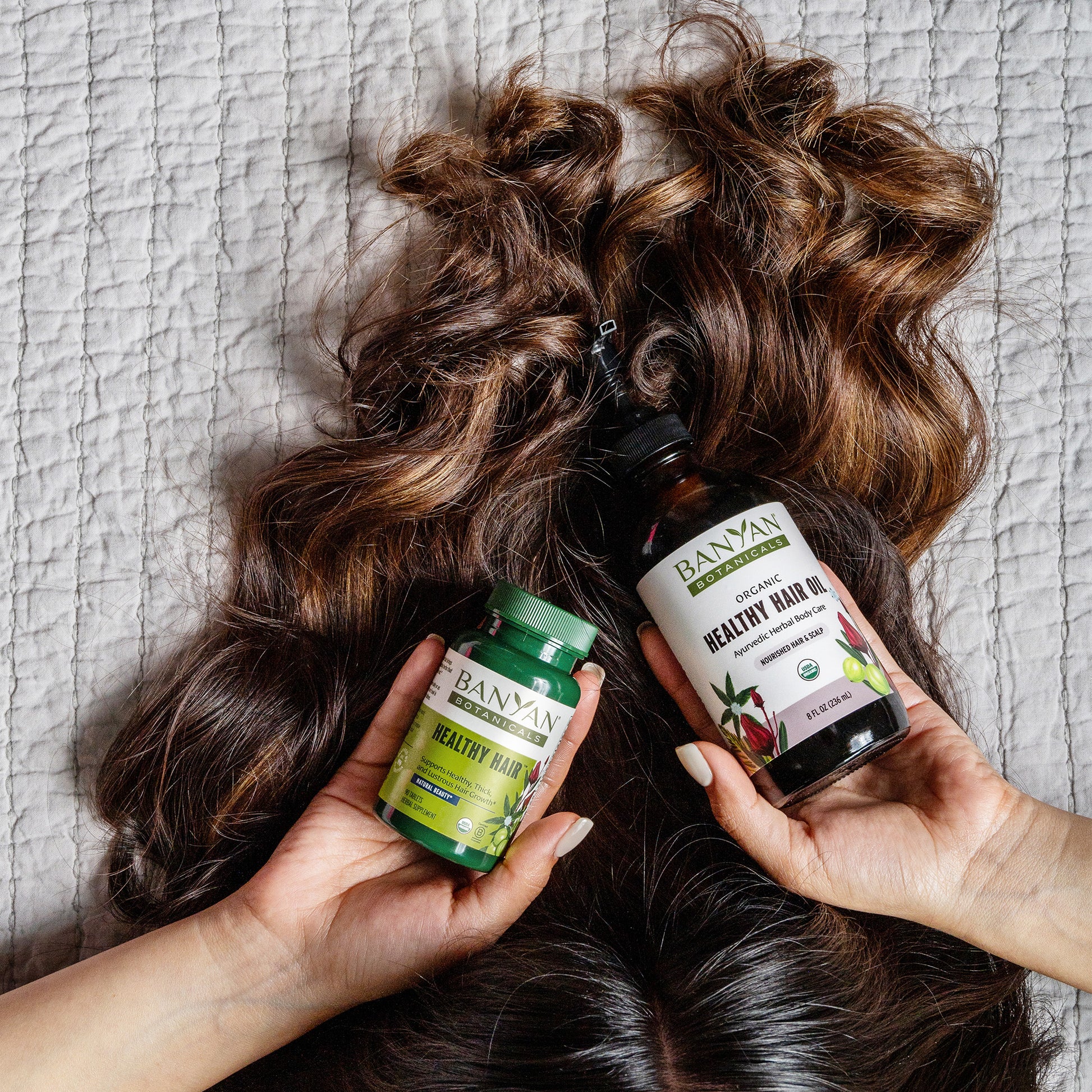 Woman holding healthy hair tablets and healthy hair oil near hair