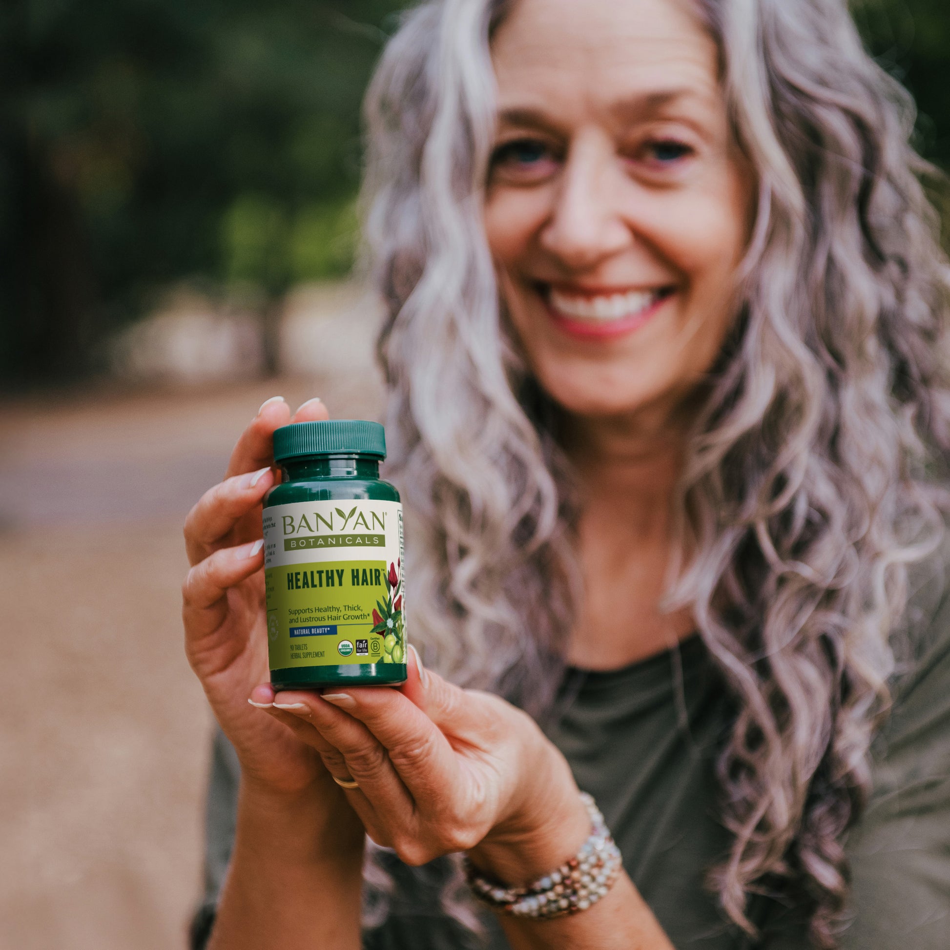 woman with thick curly hair holding bottle of healthy hair tablets